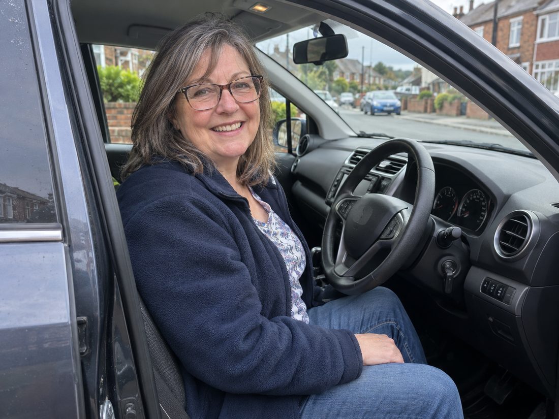 Denise, your driving instructor, smiling in the driver's seat of her car